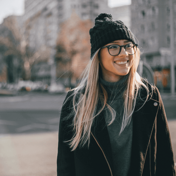 Blonde woman in city wearing glasses, coat and beanie